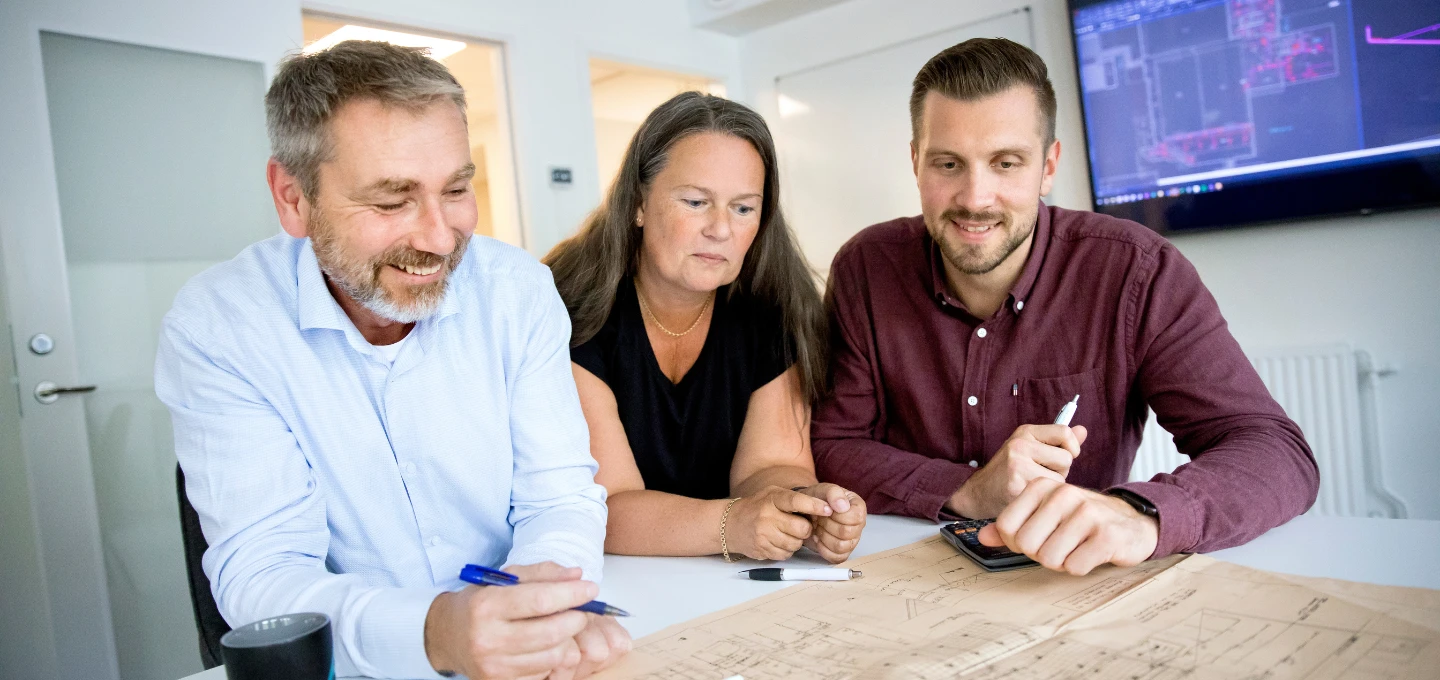 Tre personer i ett mötesrum som går igenom ritningar och projektunderlag för sprinklersystem.