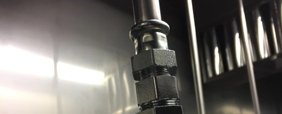 Närbild av en metallisk rörkoppling monterad i en blank teknisk miljö.